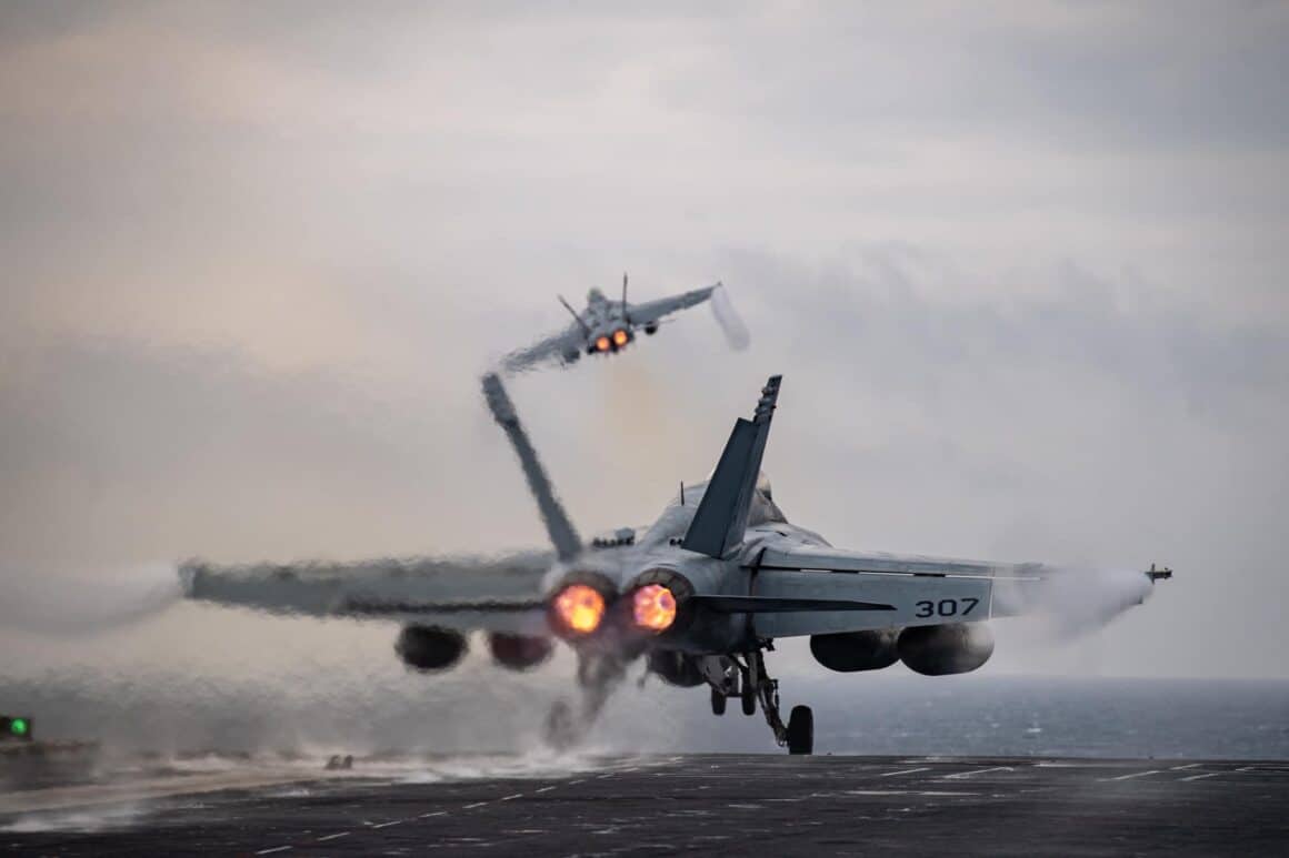 A pair of F/A-18 Super Hornets launch from the flight deck of the USS Nimitz