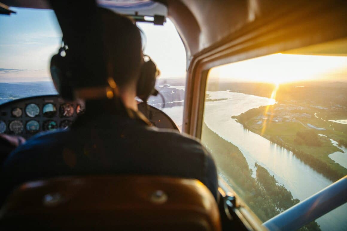 Pilot in the cockpit flying over a river at sunset